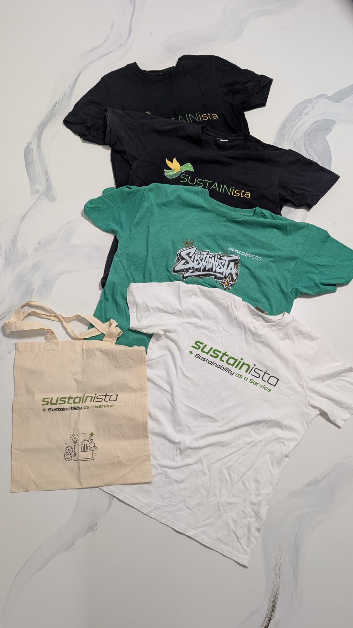 Sustainista Merch-Evolution: T-Shirts und Totebag mit verschiedenen Logo-Generationen